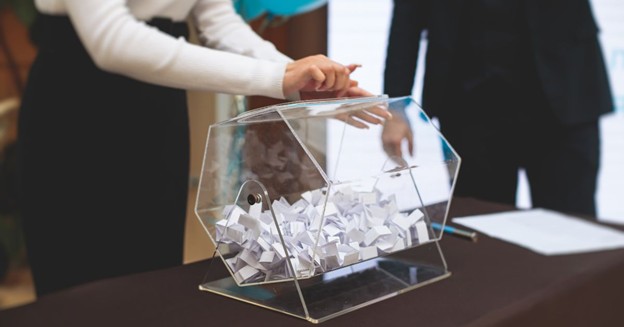 Person turning a clear raffle drum filled with entry slips on a table