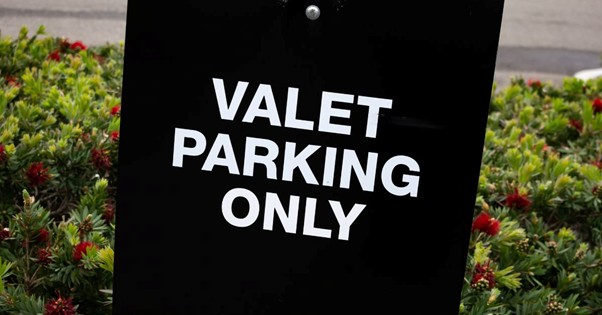 Black sign reading Valet Parking Only near landscaped bushes