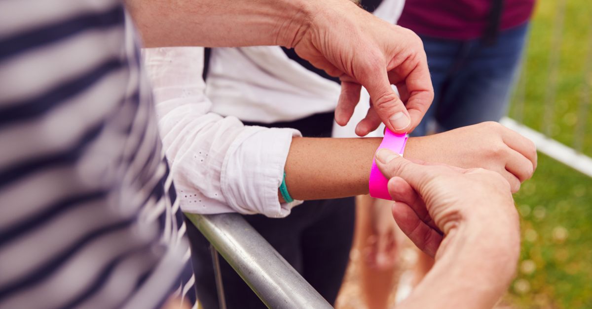 Event staff securing a bright pink wristband on a guest at the entrance rail