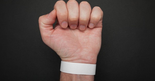 Close-up of a white event wristband on a person’s wrist with a black background