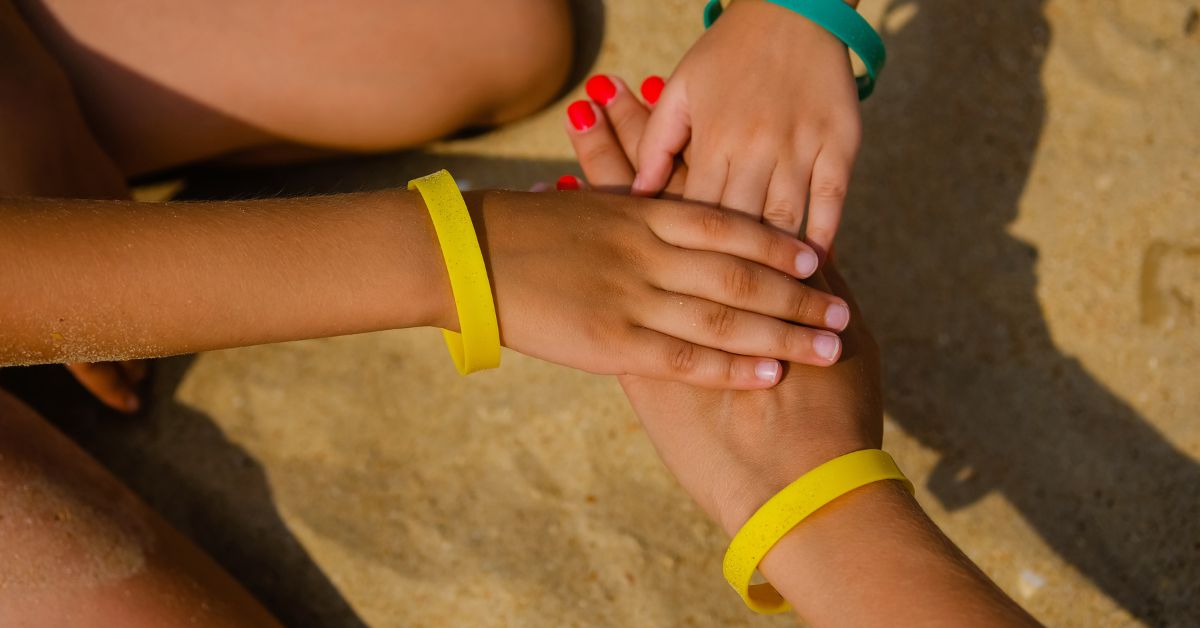 Stacked hands wearing yellow silicone wristbands on a sandy outdoor surface