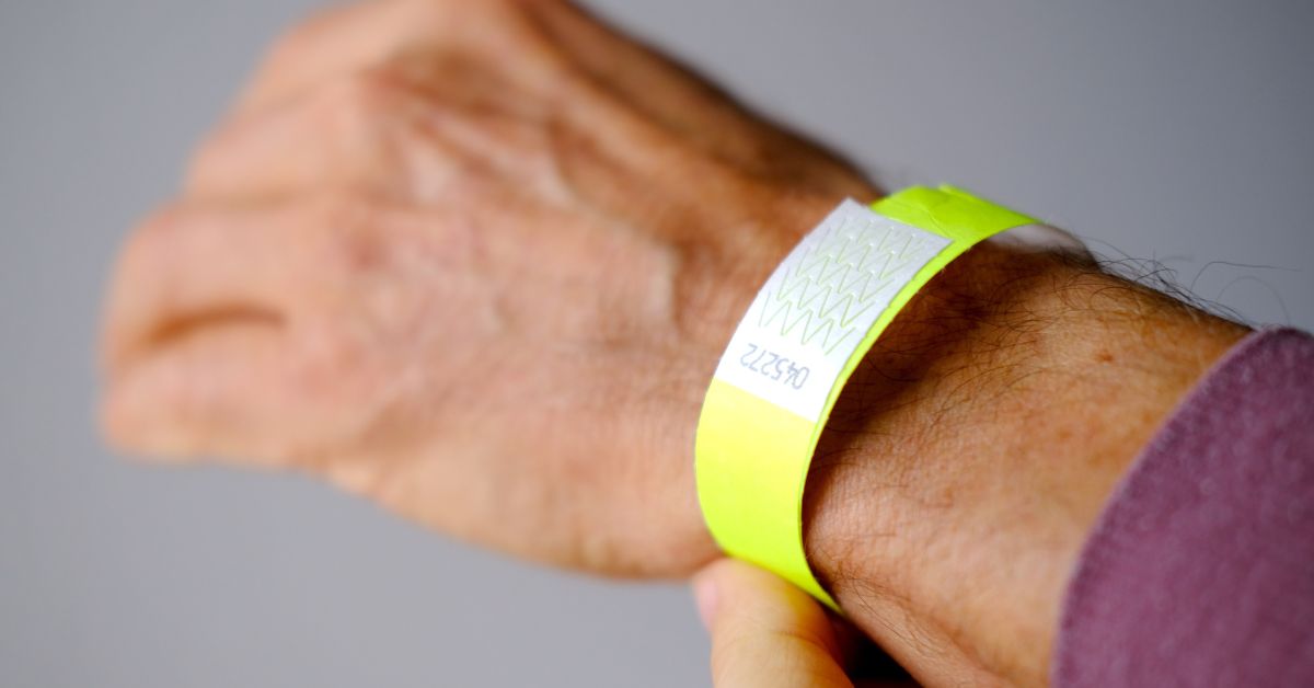 Close-up of a neon Tyvek wristband being secured on a guest’s wrist, showing the tamper-evident tab and serial number