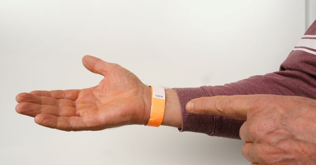 Hand wearing an orange Tyvek wristband while someone points to the closure tab