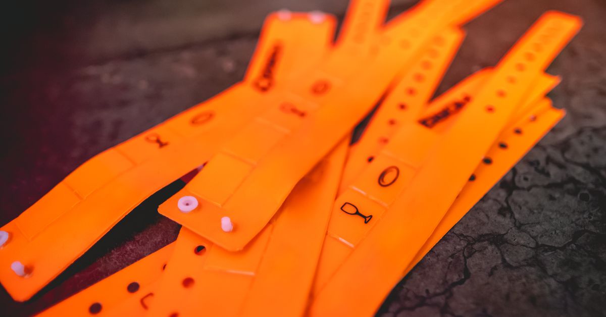 Stack of orange plastic wristbands with printed icons and snap closures